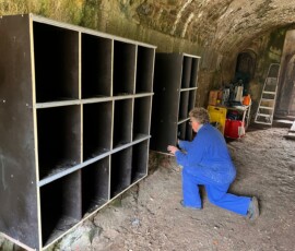 Finalisation de l'installation des casiers de rangement des casques de chantier. Un bénévole termine la fixation d'un système de casiers de rangement pour les casques des bénévoles dans un bâtiment de l'île du Large