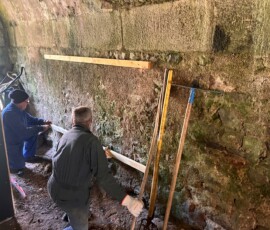 Préparation de la fixation des rangements pour les équipements de sécurité des bénévoles Deux bénévoles préparent la fixation d'une étagère de rangement des casques de chantier dans un des bâtiments du fort de l'île du Large Saint Marcouf.