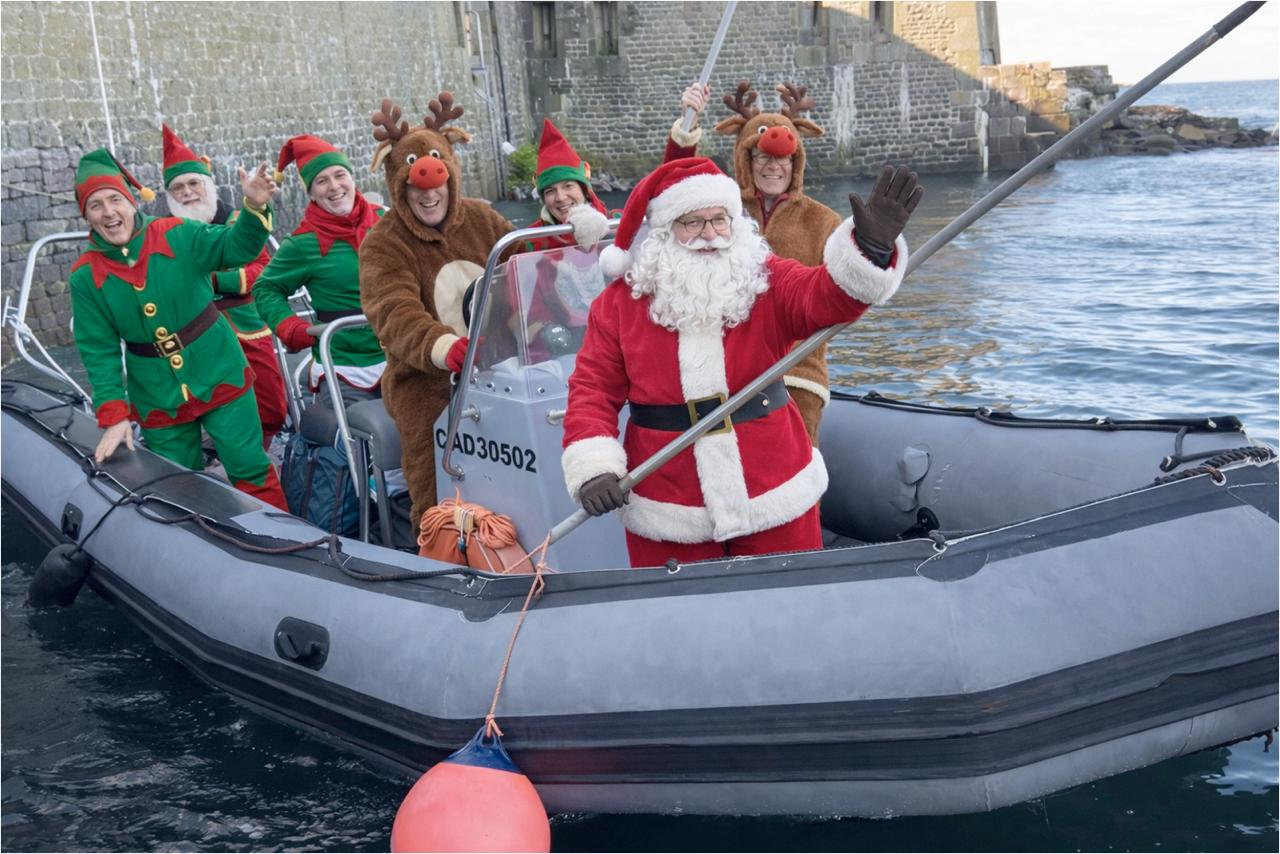 Un groupe de lutins accompagne le père Noël sur un semi rigide dans le port de l'île du Large Saint Marcouf (photomontage généré par IA)
